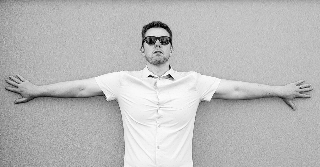 Tim Horan photographed against a concrete wall with his arms stretched wide.